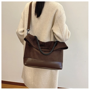 Detail of dark brown patchwork tote bag with suede texture and woven handle on model