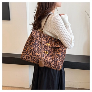 Detailed view of leopard print tote bag with brown leather trim and gold metal buckles