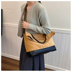 Detail of contrast stitching and woven rope handles on a brown suede tote bag