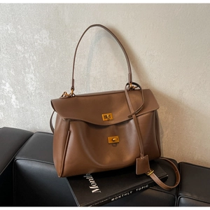 Détail du sac cabas en daim marron café avec deux fermoirs rotatifs dorés sur sofa