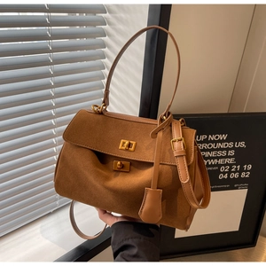 Détail d'un sac à main en daim caramel avec fermoirs rotatifs dorés et poignée en cuir