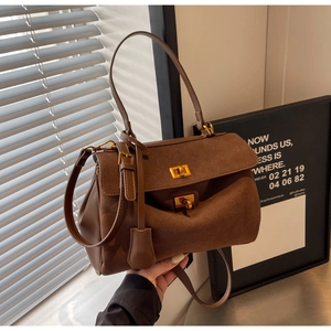Détail d'un sac à main marron en daim et cuir avec fermoir doré et accessoire décoratif