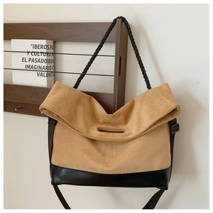 Detail of tan suede tote bag with black leather base and knotted handle on wooden rack