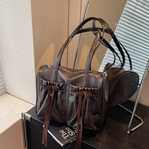 Vintage dark brown tote bag with bow details and front pleats on a black cabinet