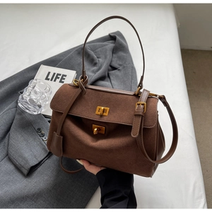 Détail d'un sac vintage en daim marron avec fermoir doré sur fond de veste grise