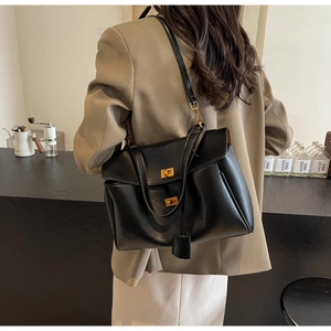 Détail d'un grand sac bandoulière en daim noir avec fermoir doré porté par un mannequin
