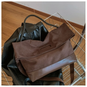 Detail of brown suede tote bag with black braided handle and wide textile shoulder strap