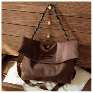 Detail of dark brown suede tote bag with textured rope handles on a vintage wooden cabinet