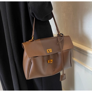 Détail d'un sac à bandoulière en daim marron avec double fermoir rotatif et breloques rétro