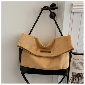 Detail of camel suede and black leather tote bag with unique cutout handle on white door
