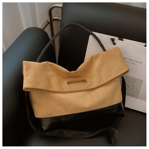 Detail of a minimalist two-tone tote bag with braided handles on a stylish leather chair