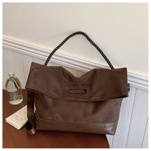 Detail view of brown suede tote bag with twisted handle and wide strap on wooden table