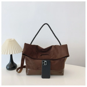 Detail of dark brown suede crossbody bag with twisted handle and phone for scale