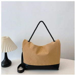 Detail of camel suede tote bag with black leather base and rope handle on white desk