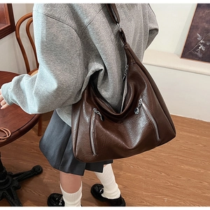 Detail of a large brown oil wax leather tote bag with decorative zippers and a wide strap