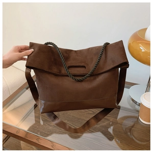 Detail of coffee brown tote bag with suede upper and smooth leather base on glass table