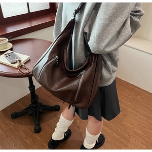 Detail of dark brown leather tote featuring front zippers and adjustable wide shoulder strap