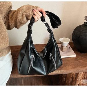 Detail of black glossy leather hobo bag with dual vertical zipper pockets and wide strap