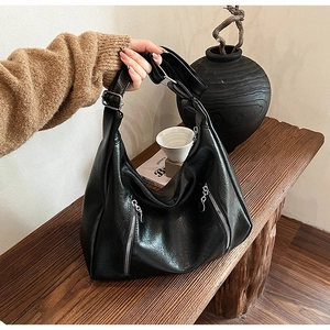 Detail of a vintage black tote bag with silver zippers on a wooden bench setting