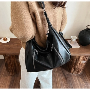 Detail of a black large capacity leather hobo bag with silver zippers shown on model