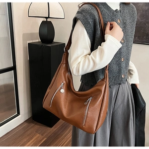 Brown leather large crescent tote bag with silver zippers shown on a model
