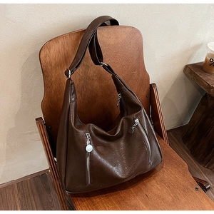 Detail of vintage brown PU leather hobo bag with dual vertical silver zippers on a chair