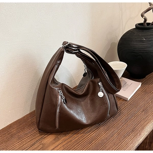 Detail of a large vintage brown shoulder bag with silver zippers on a wooden table