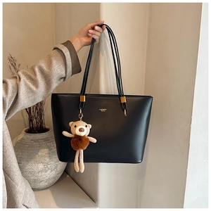 Detail of black matte leather tote bag with gold logo and cute bear plush charm