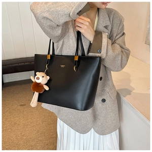 Detail of minimalist black tote bag featuring gold hardware and plush bear charm accent