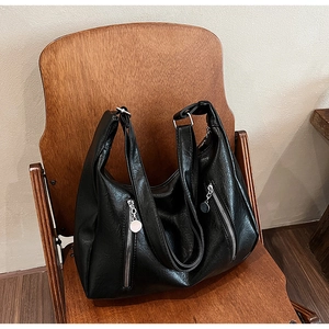 Detail of a large black vintage tote bag with vertical zippers on a wooden chair