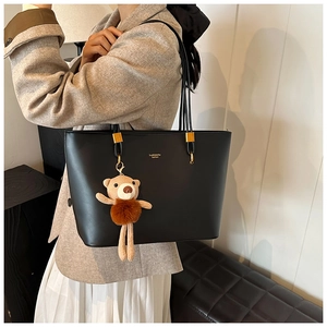 Close-up of black leather tote bag with teddy bear charm and gold hardware on model