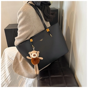 Detail view of black tote bag with gold lettering and cute brown bear plush charm