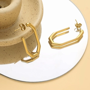 Dettaglio di orecchini geometrici placcati oro 14K su una superficie riflettente a specchio