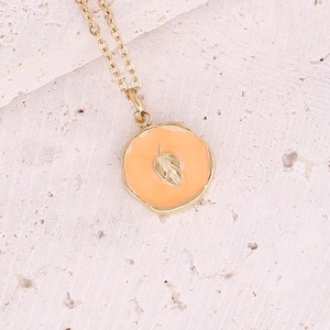 Collana dorata con pendente in smalto arancione e dettaglio foglia su fondo pietra