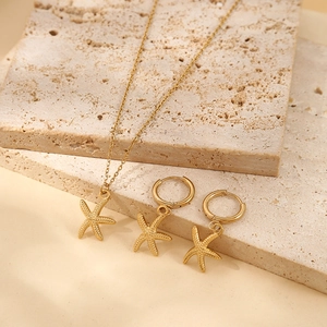 Gold starfish pendant necklace and hoop earrings set on beige textured stone base