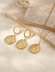 Détail de boucles d'oreilles et collier dorés avec motif texturé sur pierre beige