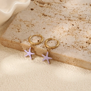 Close-up of golden starfish pendant earrings with lavender enamel finish on a stone surface