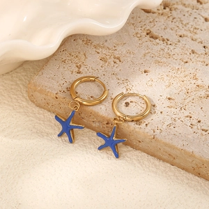 Detailed shot of gold starfish earrings with blue enamel finish on a stone surface