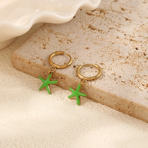 Detail of gold hoop earrings with vibrant green enamel starfish charms on stone surface