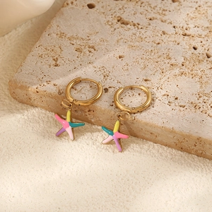 Detailed shot of gold hoop earrings with colorful starfish charms on a stone texture