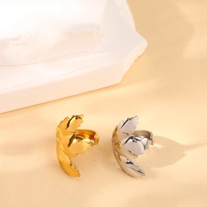 Polished leaf-shaped stainless steel rings in gold and silver finish on a stone pedestal
