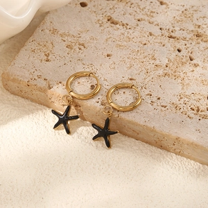 Close-up of golden starfish hoop earrings with black enamel finish on a stone display
