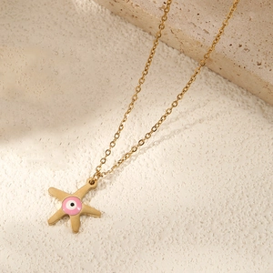 Gold starfish necklace with evil eye pendant on a warm natural stone background