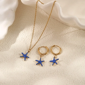 Golden stainless steel starfish jewelry set with blue charms on a beach background
