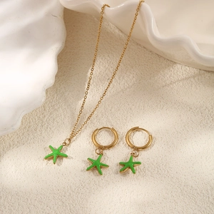Detail of gold necklace and hoop earrings with green enamel starfish pendants on shells
