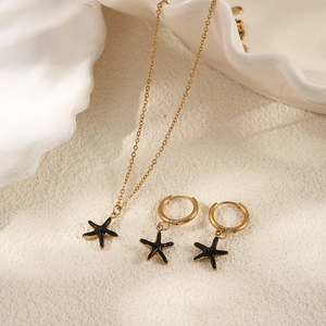 Detail view of gold starfish jewelry set with black enamel on a textured surface