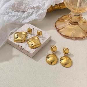 Détail de boucles d'oreilles dorées irrégulières sur pierre texturée et papier blanc