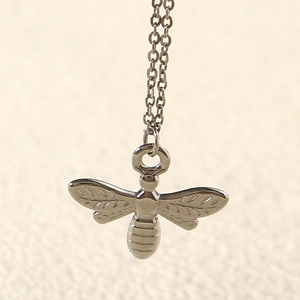 Macro detail of a 3D silver bee pendant featuring textured wings and a polished link chain