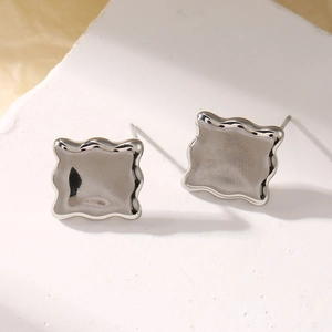 Macro detail of silver wavy square stud earrings on white textured stone background