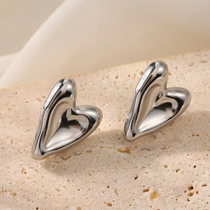 Close-up of polished silver heart stud earrings resting on a textured stone base